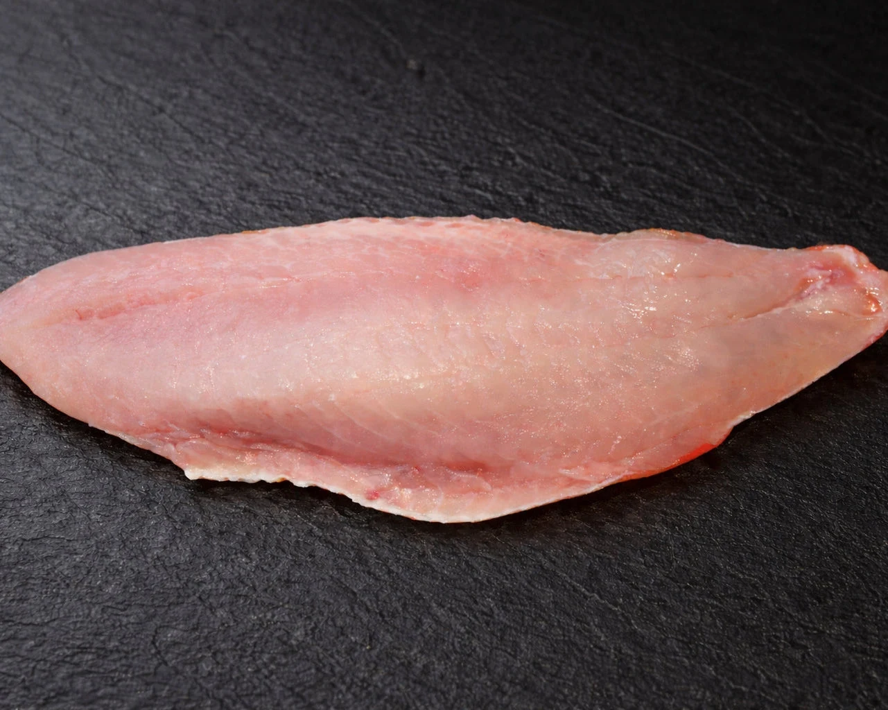 Fersk uerfilet med rosa skjær i kjøttet og rødt skinn, lagt på mørk skiferplate i fiskedisken